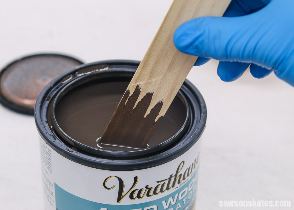 Hand using a paint stick to stir a container of Aged Wood Accelerator