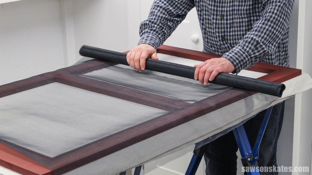 Person unrolling window screen fabric on top of a window frame