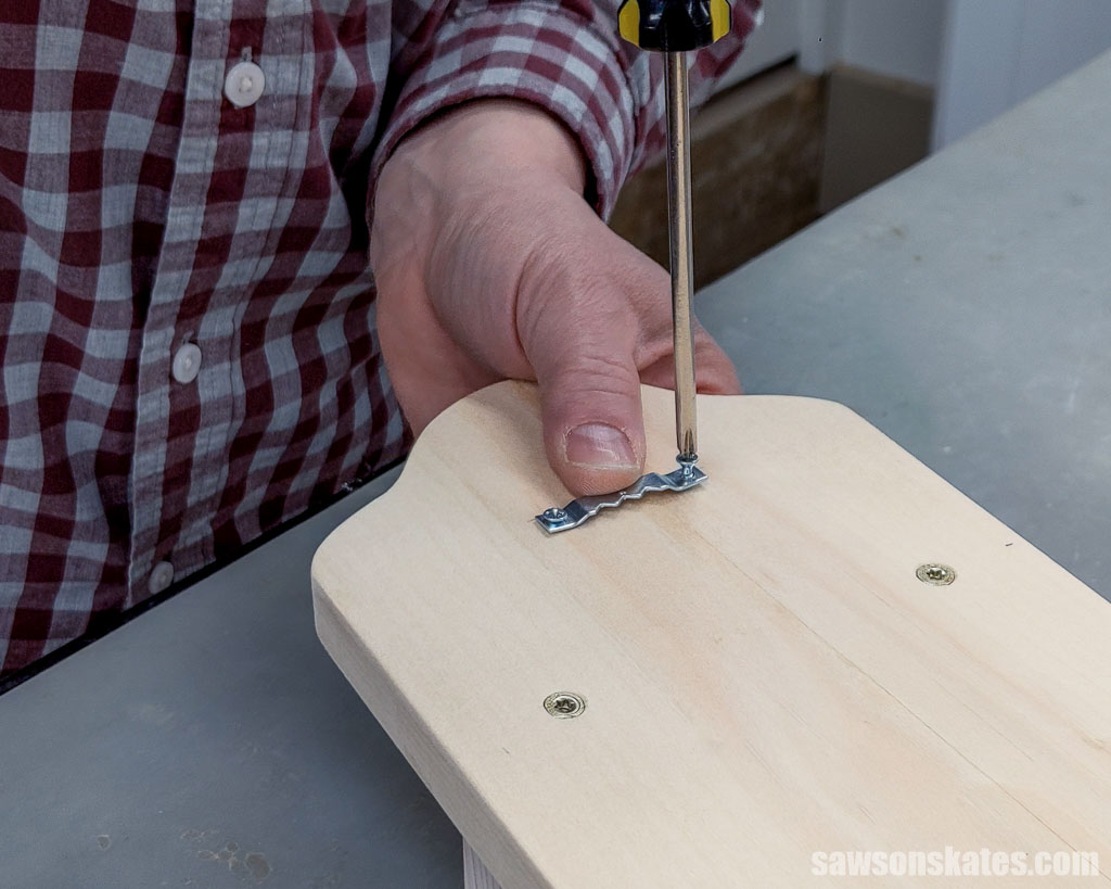 Using a screwdriver to attach a sawtooth hanger to the back of a key holder