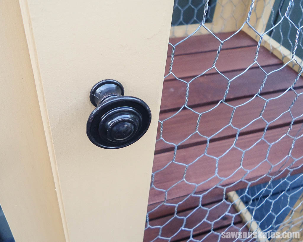 Close up of a DIY outdoor enclosed plant stand's door knob and door detail