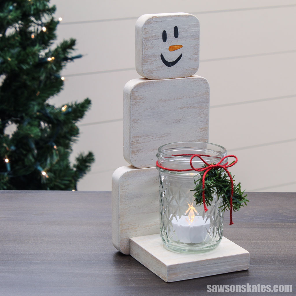 DIY wood snowman mason jar candle holder with a Christmas tree in the background