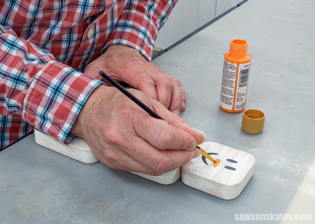 Hand using a brush to paint a DIY wooden snowman candle holder's face