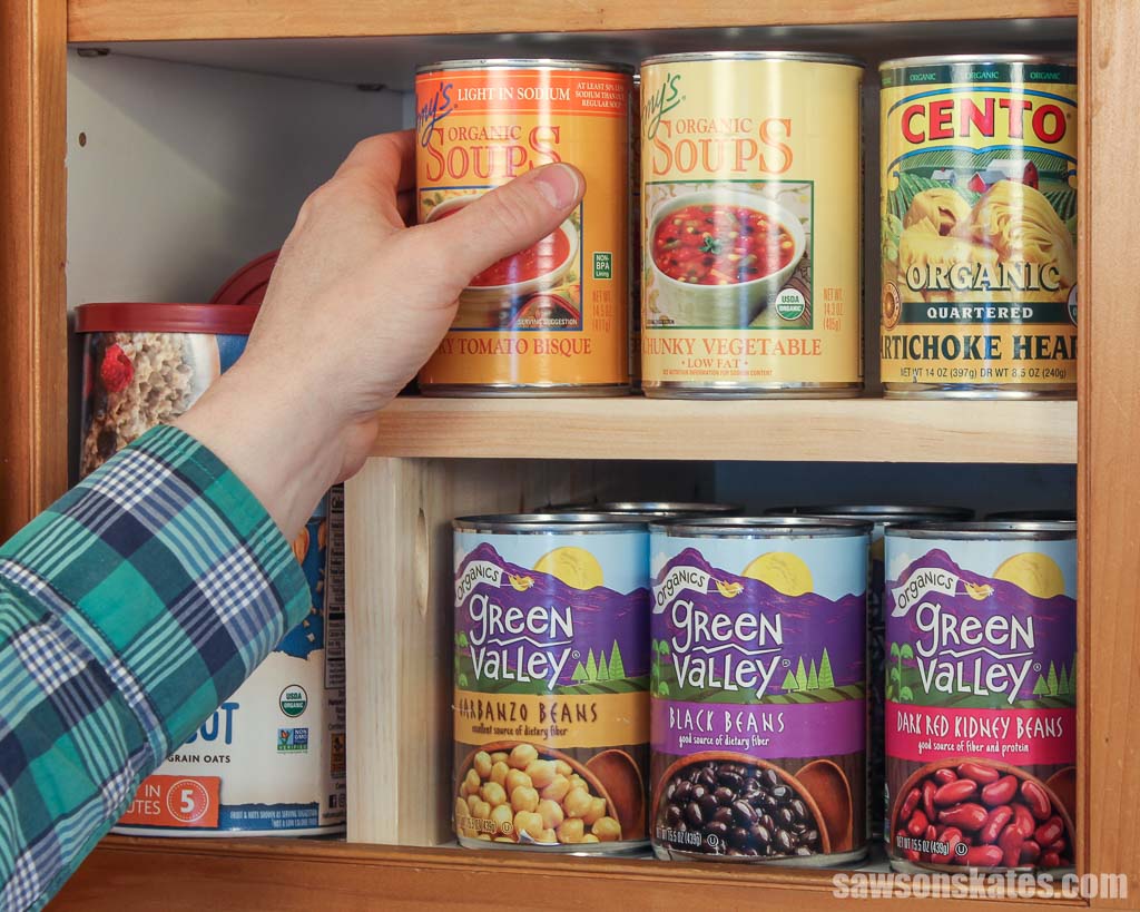 Hand removing a soup can from a simple-to-make cabinet organizer shelf