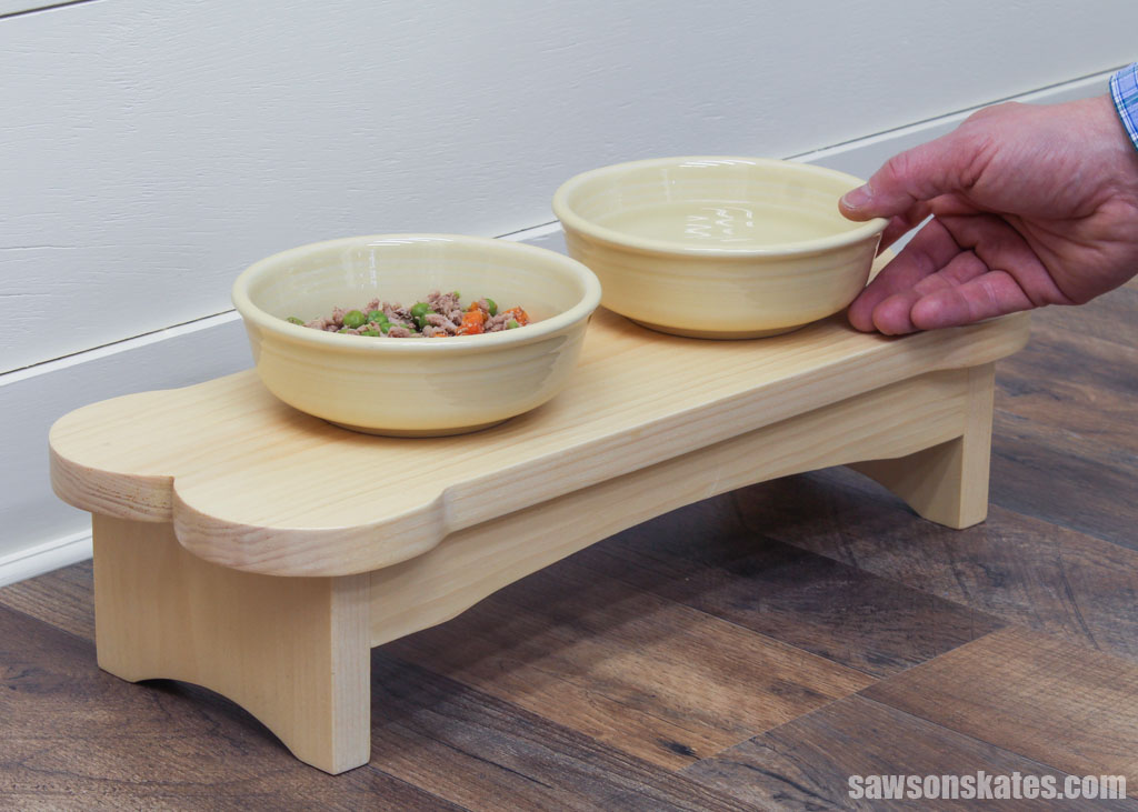 Hand placing a bowl on a simple-to-make dog food stand