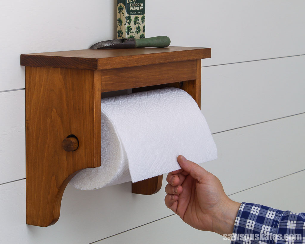 Hand pulling a paper towel from an easy-to-make wall-mounted paper towel holder