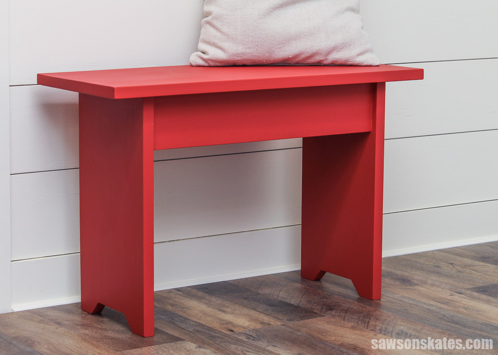 Simple red DIY bench next to a wall with a pillow on  top