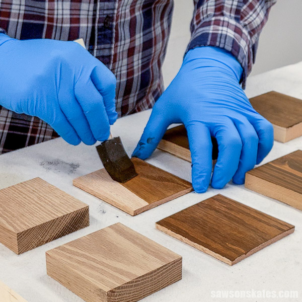 Hands covered with blue disposable gloves using a foam brush to apply wood stain