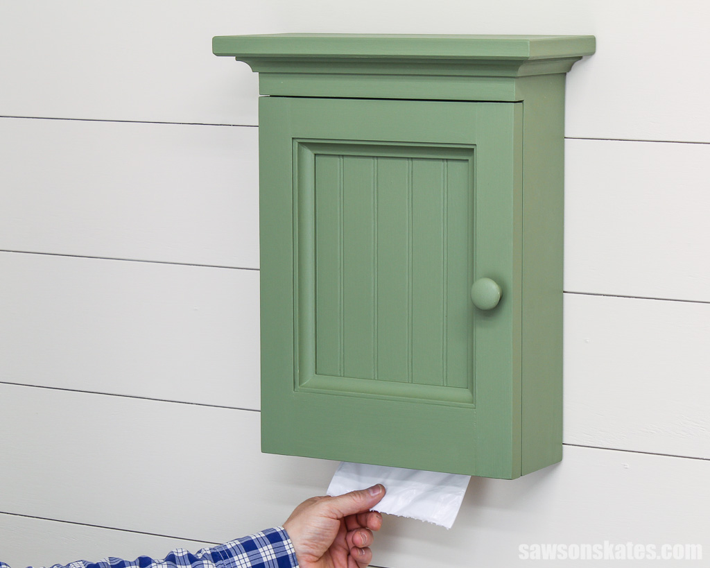 Hand pulling a garbage bag from a DIY wall-mounted trash bag dispenser