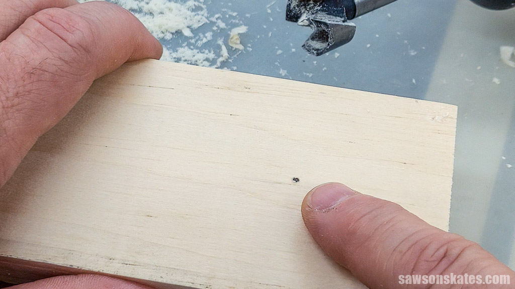 Finger pointing to a hole on the underside of a board made by a Forstner bit's spur