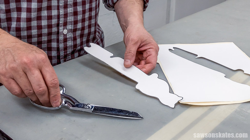 Hands holding scissors and a cat-shaped paper template for a DIY oven rack puller
