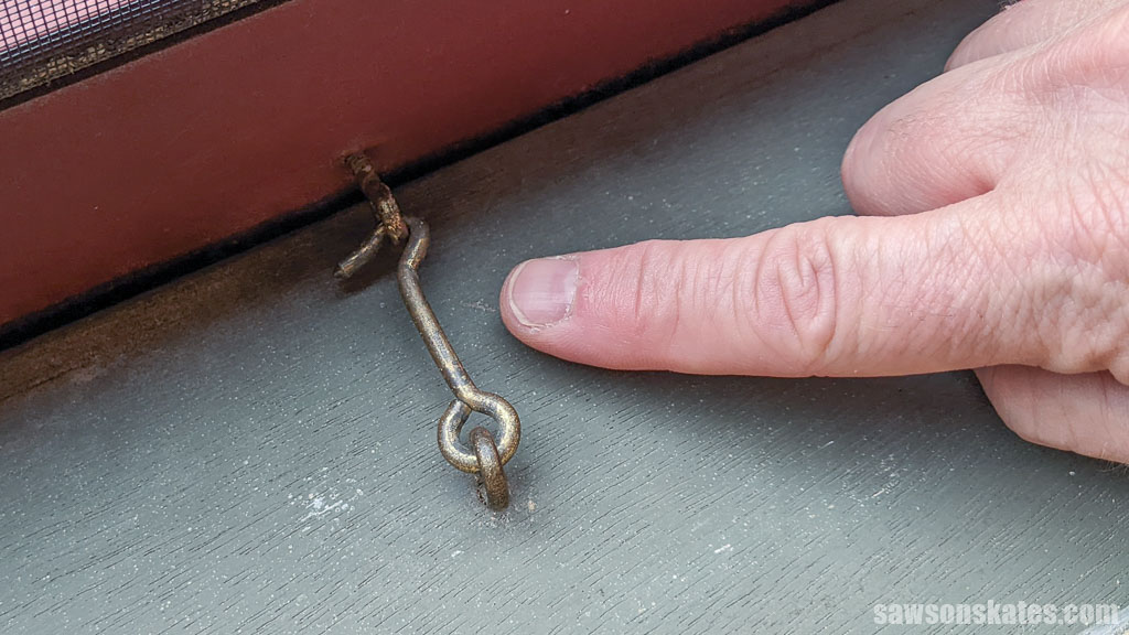 Finger pointing to a hook and eye that secures a DIY wood storm window in place