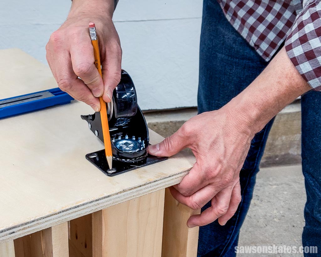 Using a pencil to trace a wheel's mounting holes onto a small DIY lumber cart's plywood bottom