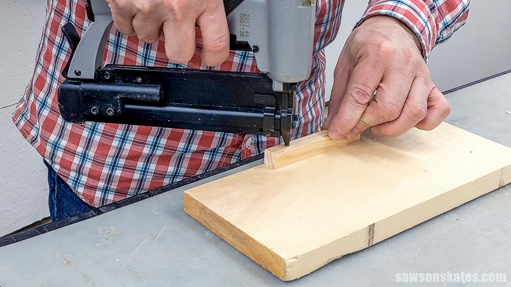 Using a pin nailer to attach a narrow piece of wood to a board