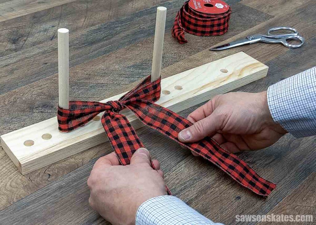 Hands tying a red plaid bow on a DIY wooden dowel bow maker