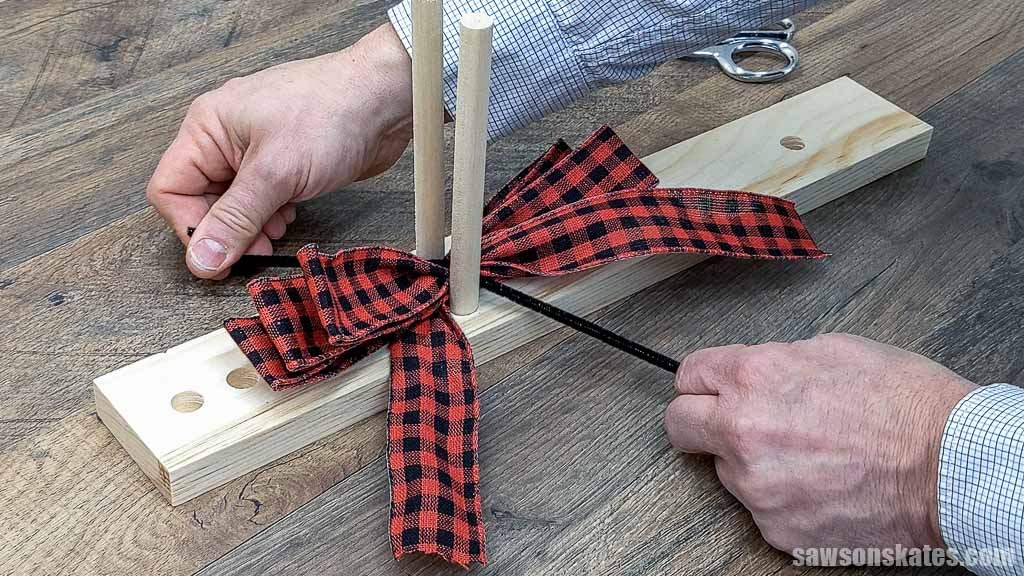 Hands cinching a multi-loop bow on a DIY wooden dowel bow maker