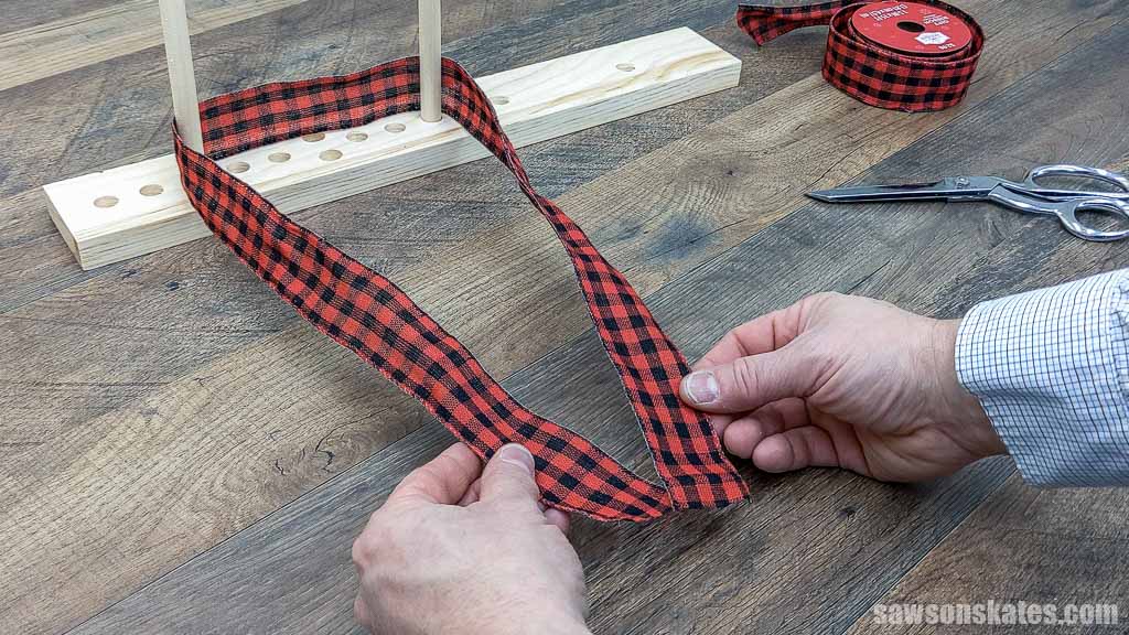 Hand's wrapping red plaid ribbon around the dowels of a DIY bow maker