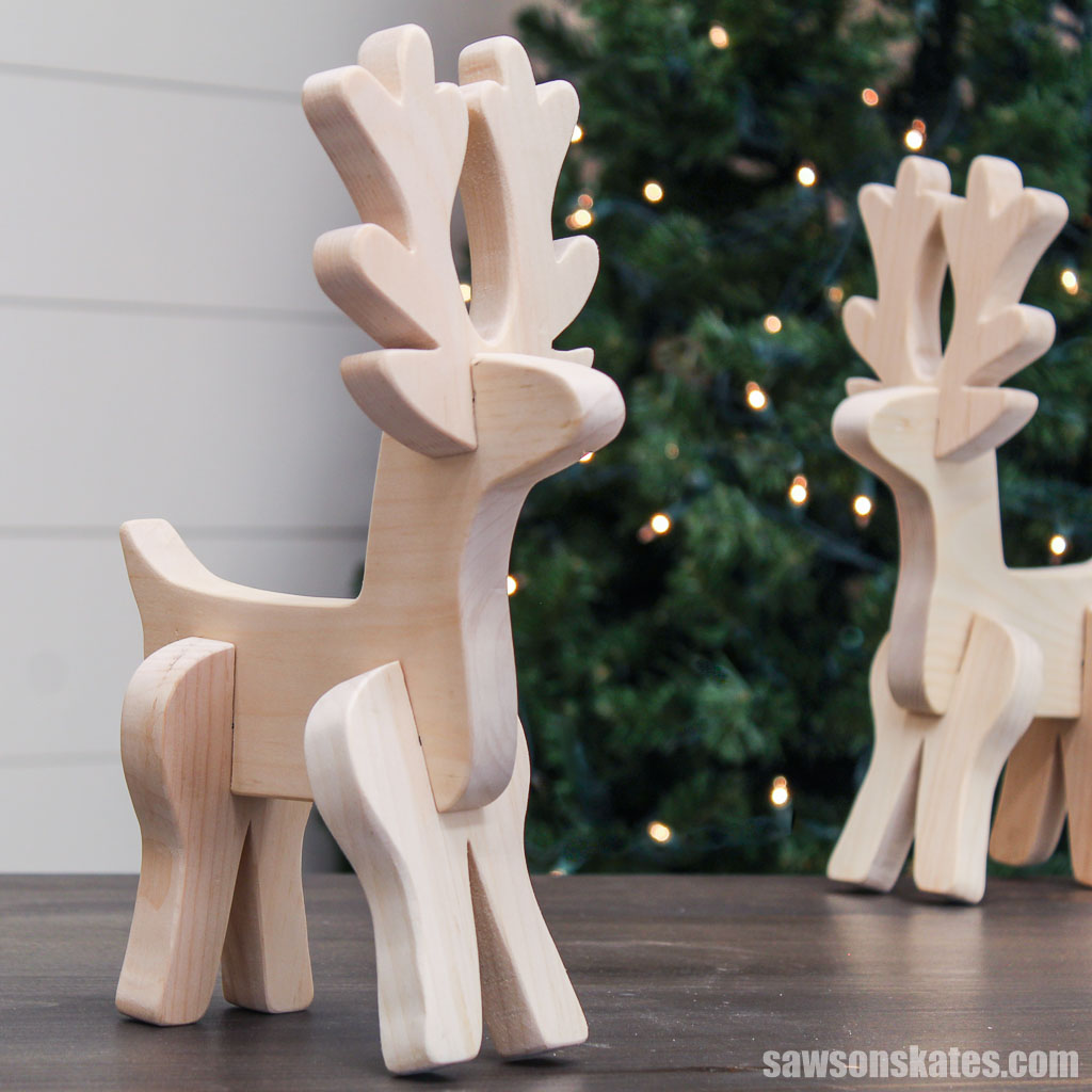Two wood DIY reindeer on a table with a Christmas tree in the background