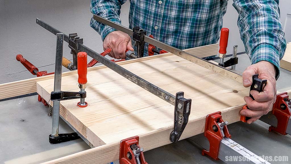 Hands tighten a clamp on a wooden panel