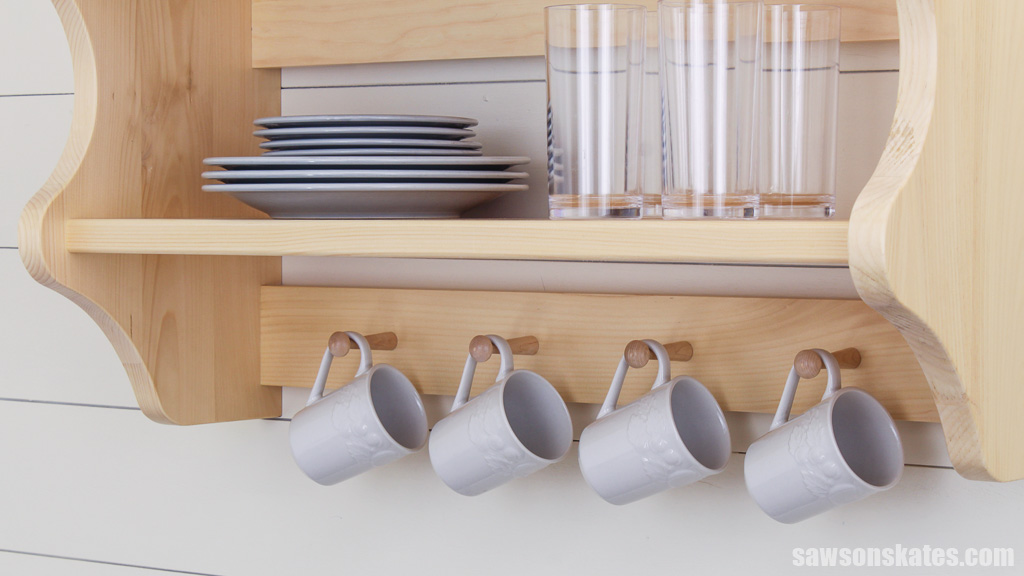 Four pegs used to display coffee mugs at the bottom of wall-mounted DIY kitchen shelves