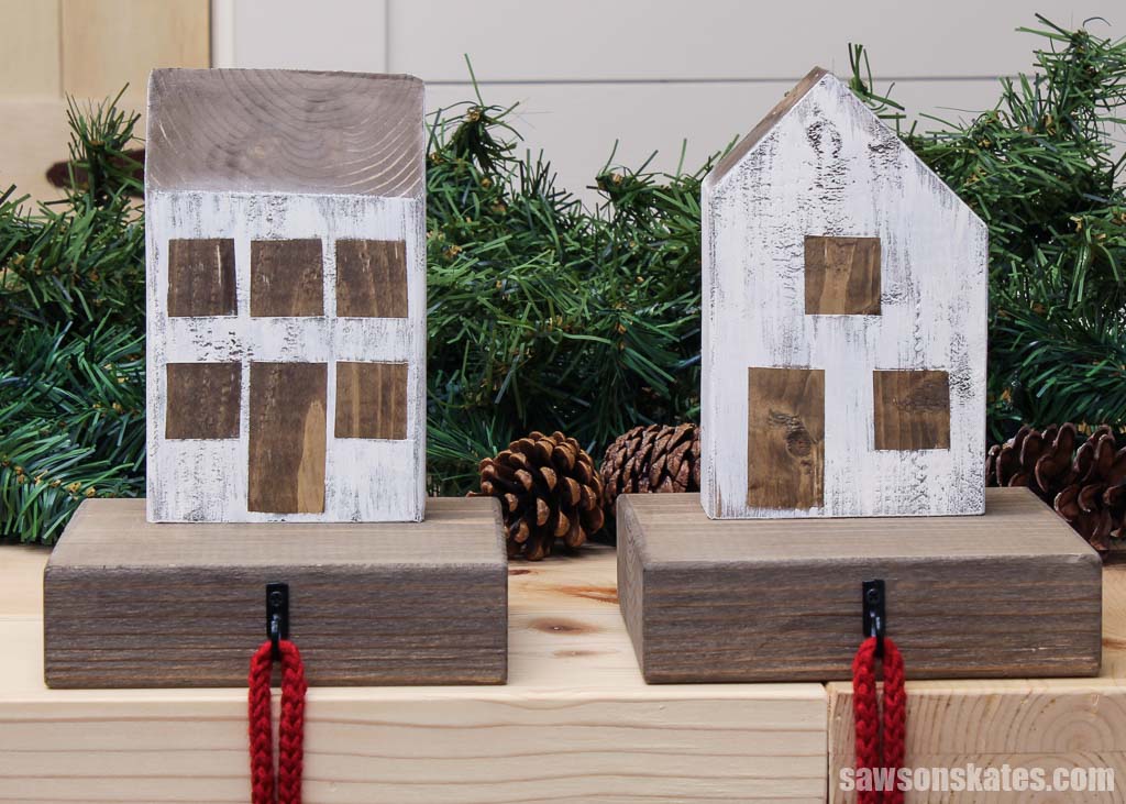 A manor and cottage style DIY wood Christmas village stocking holders with evergreens and pine cones in the background