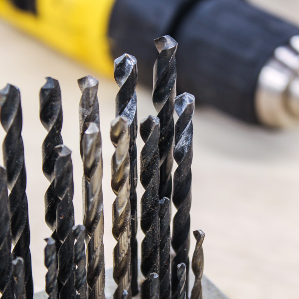 Several drill bits standing up in the foreground and a blurry drill in the background