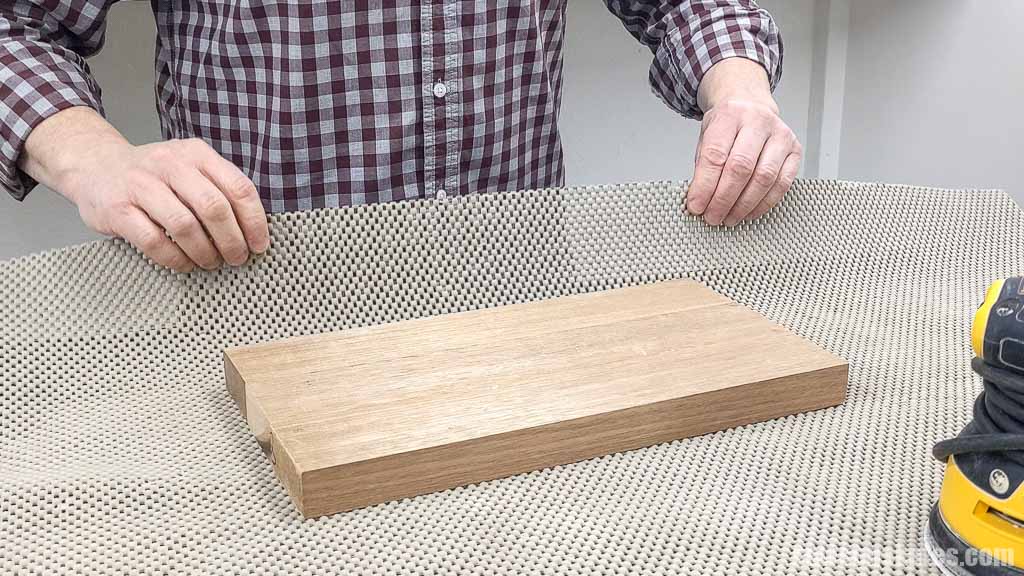 Hands picking up a non-slip mat used under a piece of wood while sanding