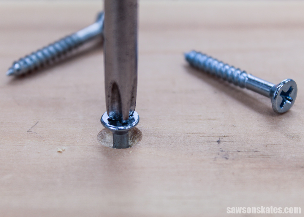 Screwdriver in the foreground driving a screw into a countersink hole with two screws in the background