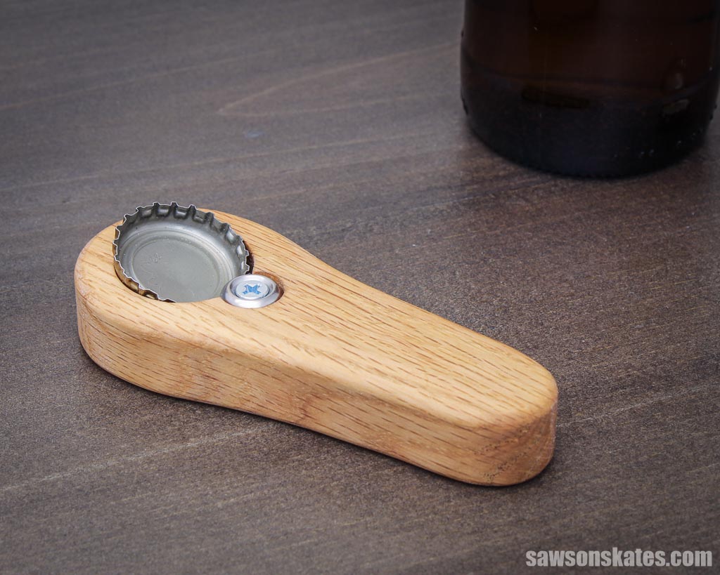Wooden DIY handheld bottle opener on a table with a bottle in the background