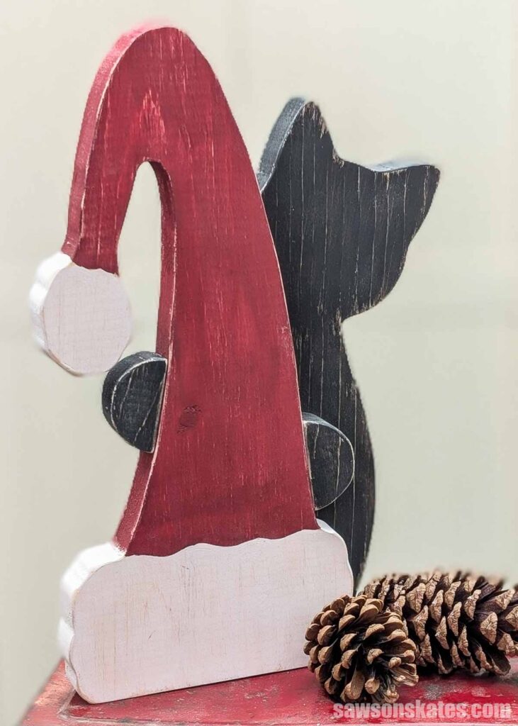 Wooden black cat peeking around a red Santa hat