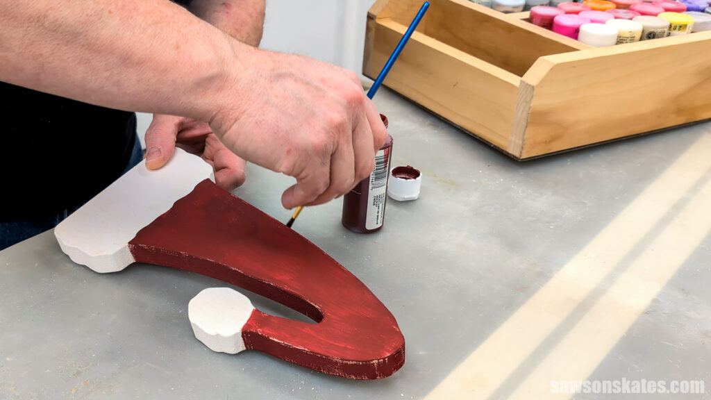 Hand using a brush to paint the side of wooden Santa Claus hat