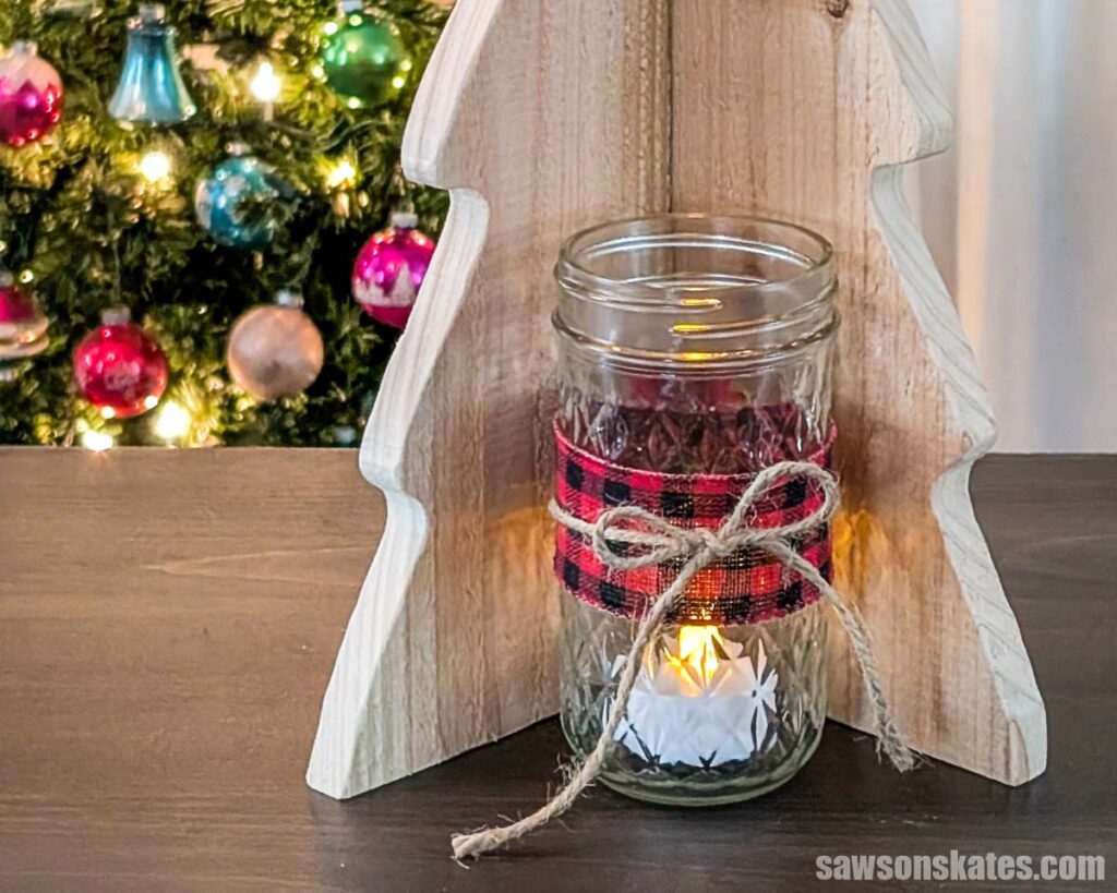 Closeup of a mason jar with an LED tea light in front of a DIY wooden Christmas tree