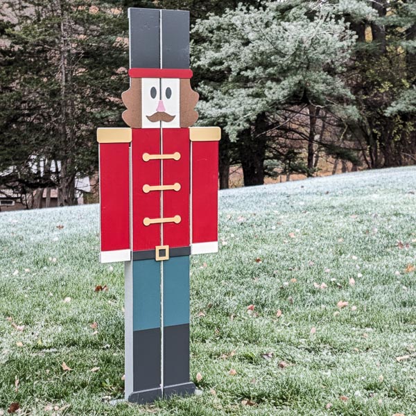 DIY wooden nutcracker yard decoration in field with a dusting of snow