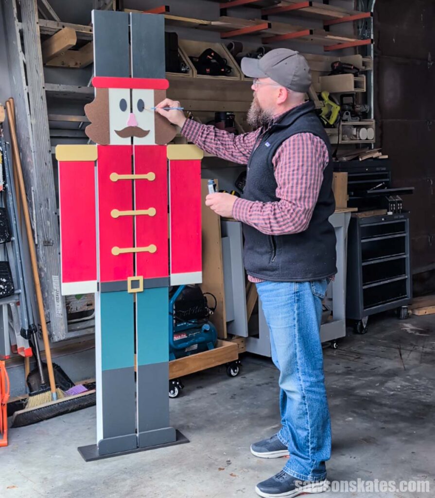 Scott using a small brush to touch up the paint on a handmade 6-foot nutcracker decoration.