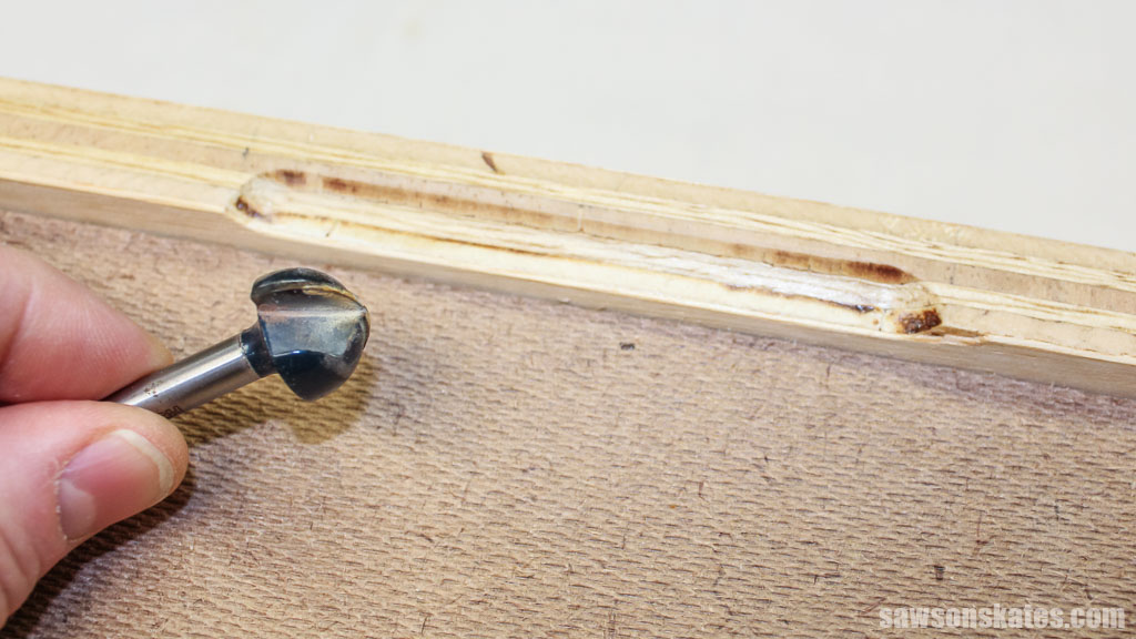 Fingers holding a router bit next to a recess made by the bit