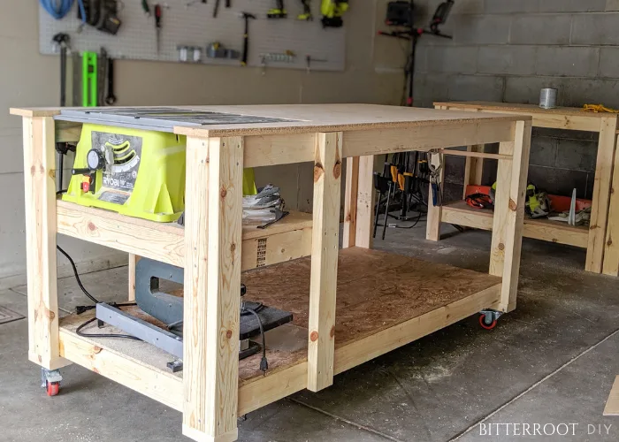 DIY table saw workbench with a built-in saw, large work surface, lower shelf, and caster wheels in a garage workshop.