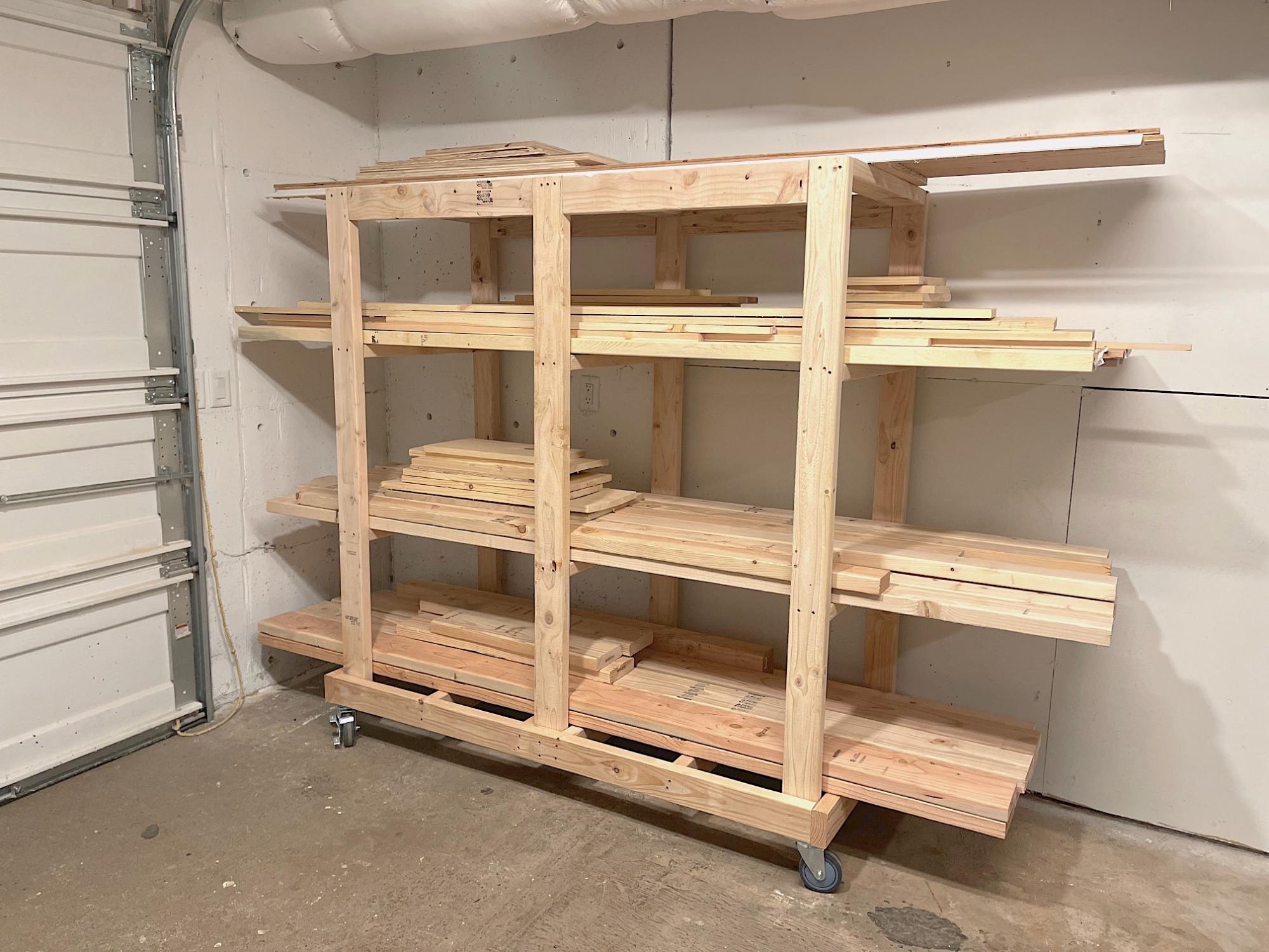 DIY rolling lumber rack with multiple horizontal storage shelves holding dimensional lumber, trim boards, and long wood offcuts in a garage workshop.