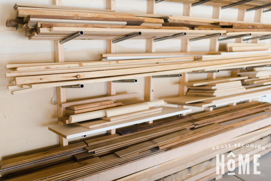 Wall-mounted lumber storage rack with horizontal metal pipe supports holding boards, trim pieces, and sheet material in a workshop or garage.
