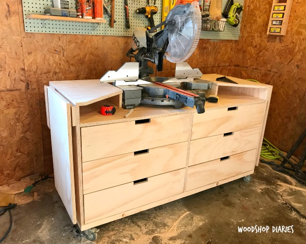 DIY miter saw stand with built-in drawers, side storage compartments, and locking casters positioned in a woodshop.