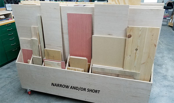 Rolling plywood scrap cart with divided vertical storage compartments holding sheet goods, plywood offcuts, and small wood scraps in a woodworking shop