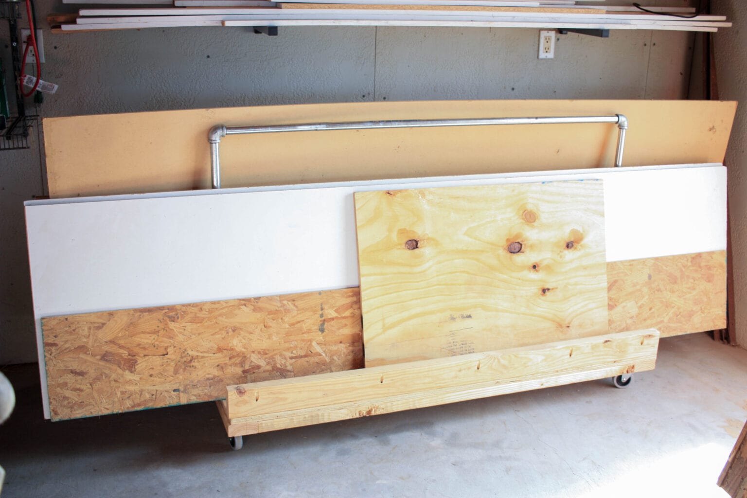 Rolling sheet goods cart holding plywood, OSB, melamine panels, and wood offcuts in a garage workshop.