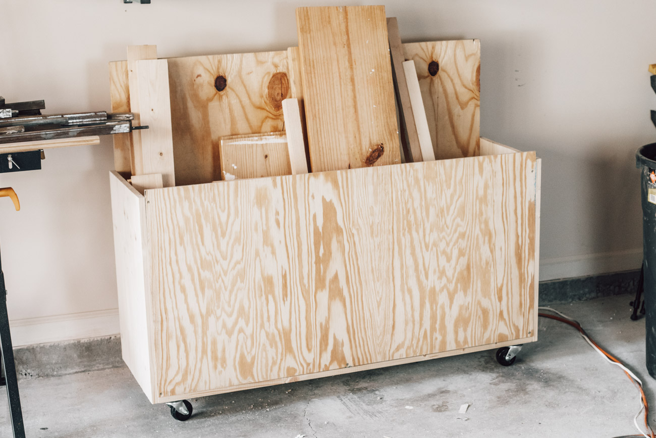 Mobile plywood scrap storage cart on casters holding sheet goods, pine boards, and wood offcuts in a garage workshop.