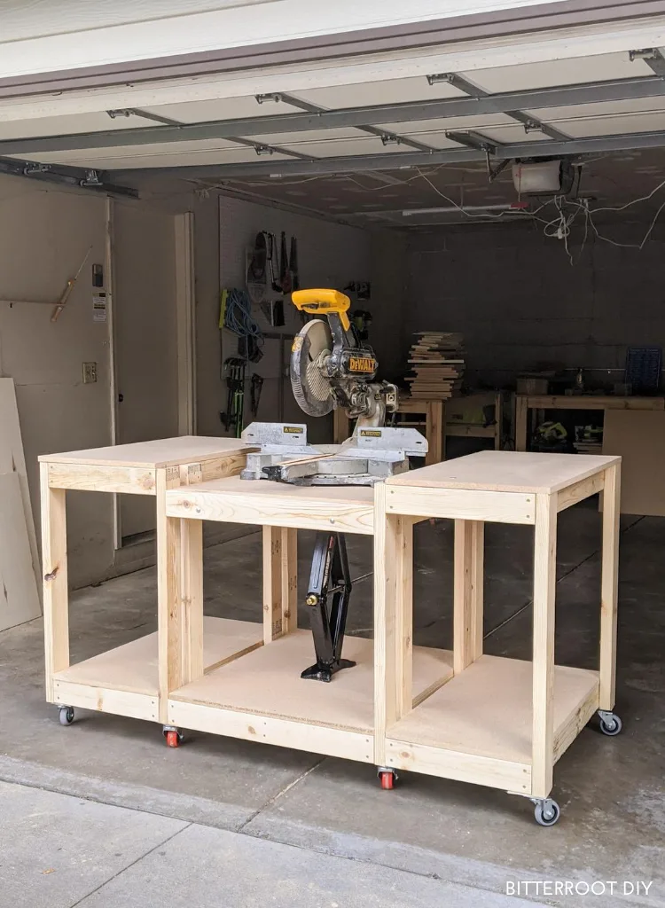 DIY workbench with integrated miter saw station, open storage bays, and locking casters positioned inside a garage.