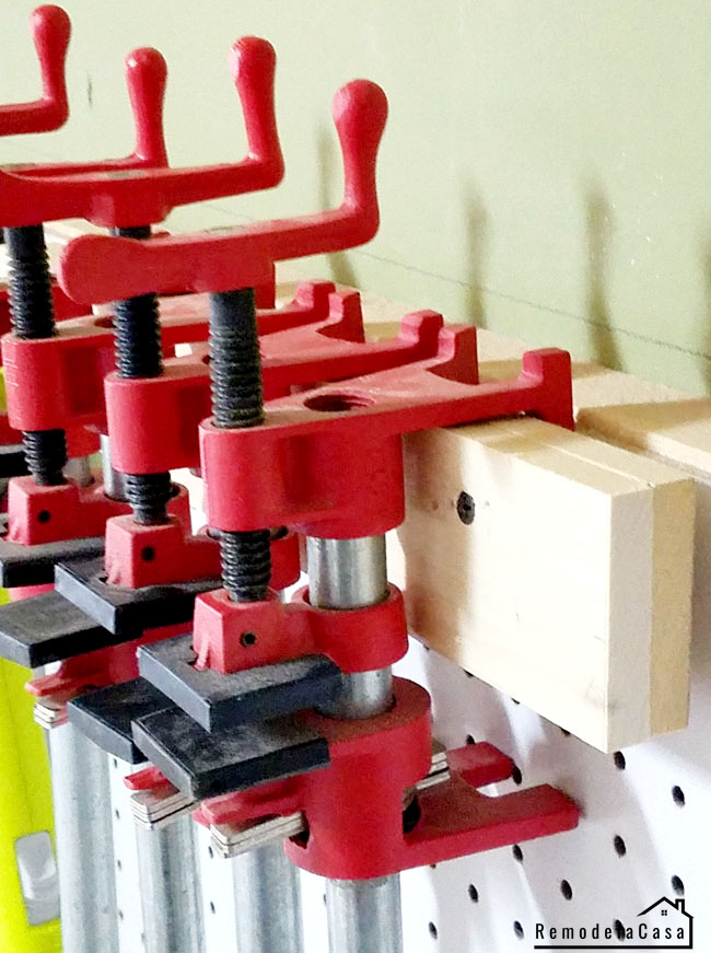 Simple DIY wall-mounted clamp holder with wood blocks for storing clamps on a pegboard wall in a compact workshop.