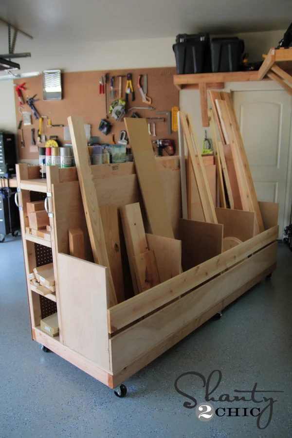 Large DIY rolling lumber cart with vertical storage compartments holding plywood sheets, hardwood boards, and scrap wood in a garage workshop.