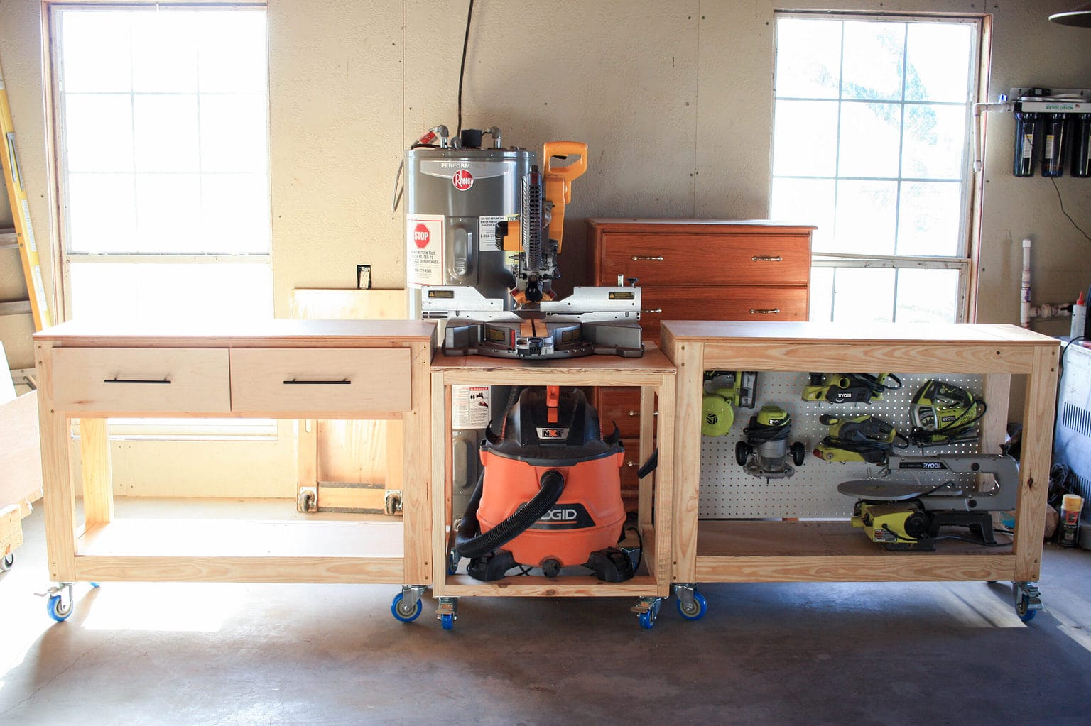 Modular DIY miter saw station with rolling workbench sections, built-in drawers, open tool storage, pegboard backing, and a shop vacuum.