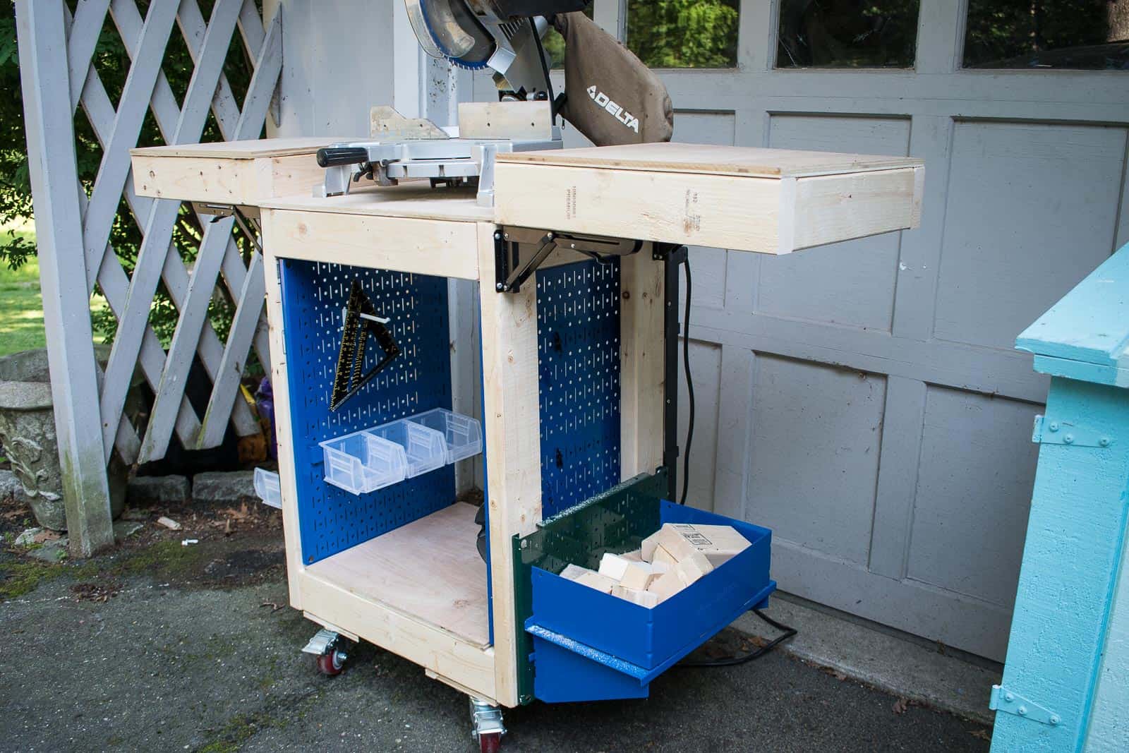 Rolling DIY miter saw cart with fold-up support wings, pegboard tool storage, side bins, and locking casters positioned beside a garage door.