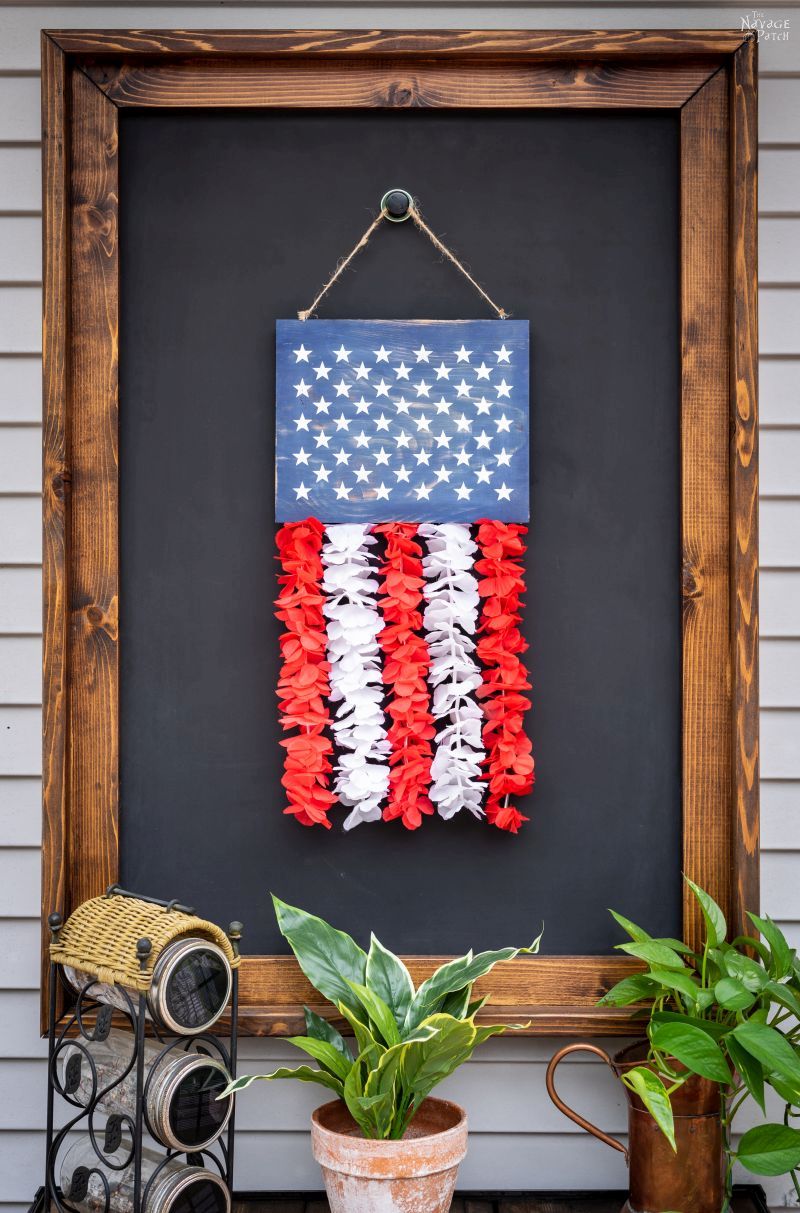 Patriotic door hanger with a blue wooden flag panel with white stars and cascading red and white fabric strips.