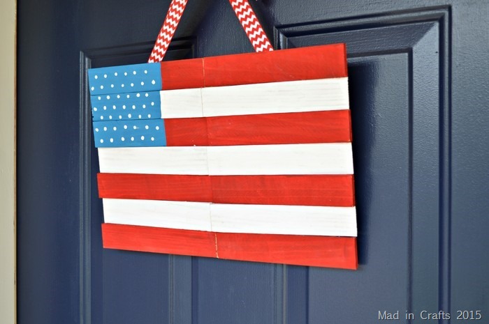 ainted American flag door decoration made from narrow wooden strips, featuring a blue field with white dots and red and white stripes.