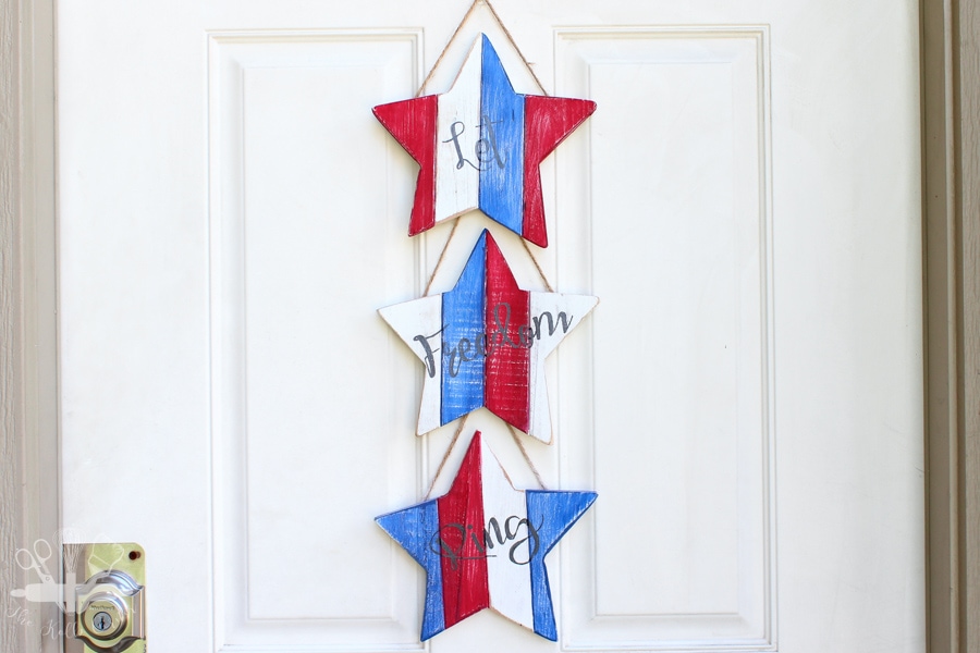 Patriotic wood star door hanger made from three painted wooden stars connected with rope and hanging on a white door.