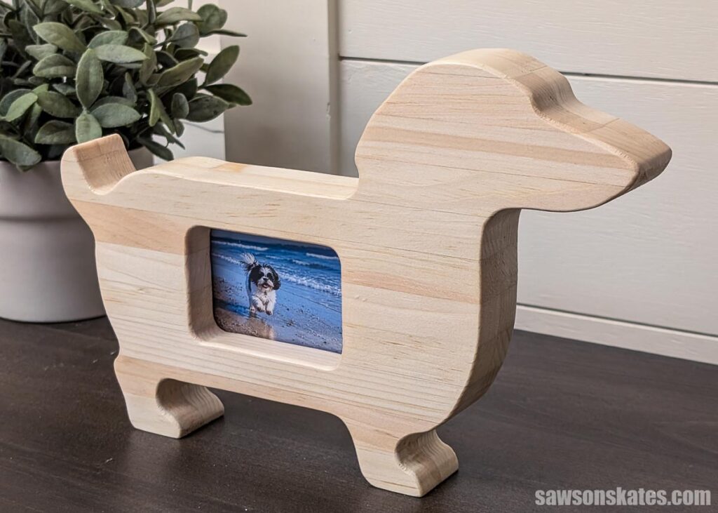 Dog-shaped wooden picture frame with a small photo of a black and white dog on the beach displayed in the center.
